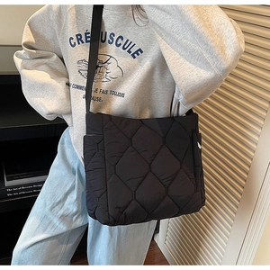 Detail view of black quilted tote bag with wide strap worn by a model in a minimal setting
