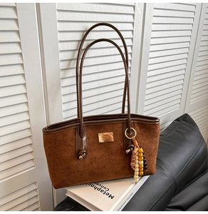Detail of dark brown faux suede tote bag featuring a gold logo plate and beaded charm