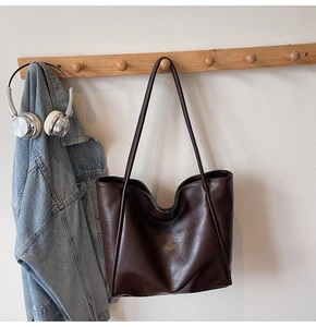 Detail view of large dark brown leather tote bag hanging on wooden hook in lifestyle setting