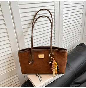Detail view of brown suede tote bag with gold logo plaque and ethnic beaded tassel charm