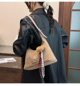 Détail du sac bandoulière en daim café avec breloque ours et plaque de marque