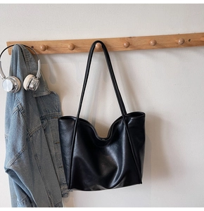 Close-up of the large black tote bag hanging on a wooden rack with a casual jacket