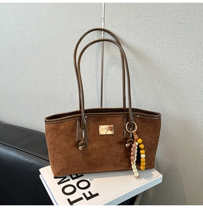 Detail of a brown suede tote bag with golden logo plaque and colorful beaded charm