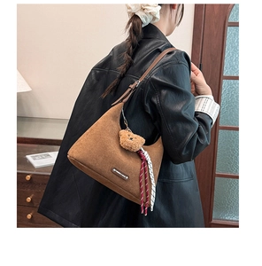 Gros plan du sac hobo en daim marron avec pendentif ours et détail de ruban rayé