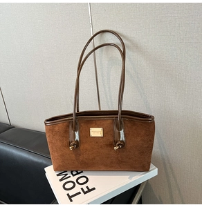 Detail of a brown suede tote bag with golden metal logo plate and decorative knots