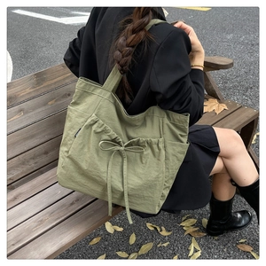 Detail of sage green canvas tote bag with drawstring bow and fashion label on the side