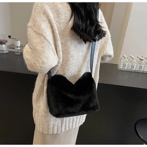 Dettaglio di una borsa a tracolla in peluche nero indossata su un maglione beige in un caffè