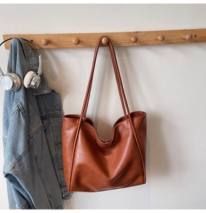 Detailed view of a brown vintage leather tote bag hanging on a wooden rack with accessories