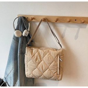 Quilted beige tote bag with rhombus patterns hanging on a wooden hook in a cozy room