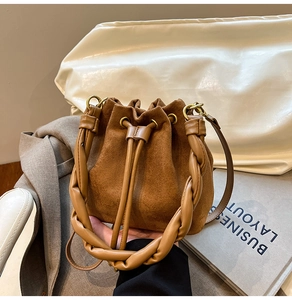 Gros plan sur un sac seau en daim marron avec une poignée en cuir tressé unique