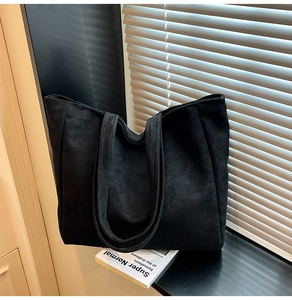 Macro detail of high-capacity black tote bag showing smooth matte texture and wide shoulder strap