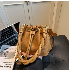 Détail d'un sac seau en daim marron avec poignée tressée et finitions en métal doré