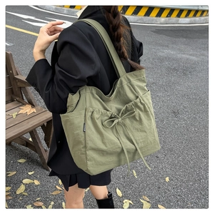 Olive green canvas tote bag with drawstring detail and side pockets worn by a model