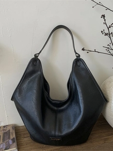Minimalist large black pebbled leather hobo tote bag with a metallic brand logo plaque