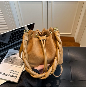 Détail du sac seau en daim marron avec poignée tressée en cuir et œillets dorés élégants