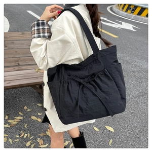 Detail of black pleated canvas tote bag featuring side pockets and a drawstring bow detail