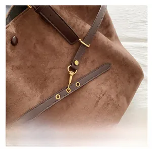Detail of brown suede tote bag featuring dark leather strap and beaded pendant charm