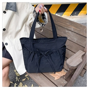 Outdoor shot of a black tote bag featuring a decorative bow and drawstring side pockets