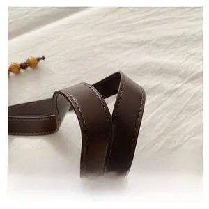 Close-up of brown leather tote handle with reinforced stitching and wooden bead detail