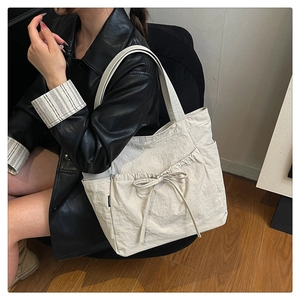 Close-up of beige canvas tote bag with bow detail and side drawstring pockets