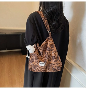Brown paisley tote bag with cloud pendant shown as a shoulder bag on a female model
