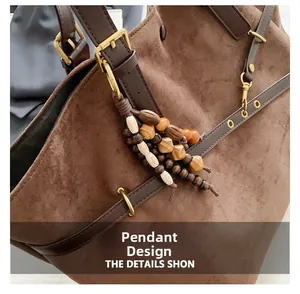 Close-up of brown suede tote bag featuring ethnic wood bead charm and gold buckle