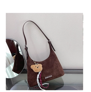 Détail du sac hobo marron foncé avec charme d'ours et cordon sur surface en verre