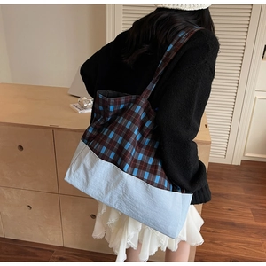 Détail d'un grand sac cabas à carreaux bleu et marron porté à l'épaule dans un intérieur