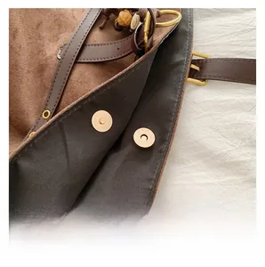 Close-up of golden magnetic snap closure and suede texture on a brown tote bag