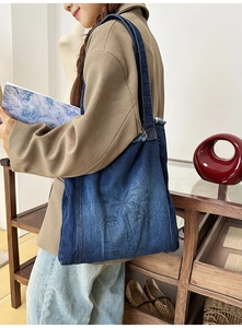 Detailed side view of a large denim tote bag with palm tree print on a shoulder strap