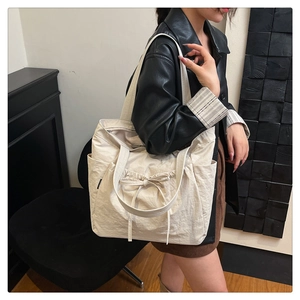 Detail of a large off-white pleated tote bag with bow drawstring and side pockets