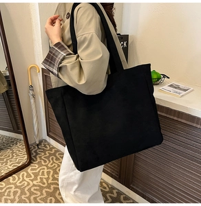Close-up of black oversized canvas tote bag with wide shoulder straps on a female model