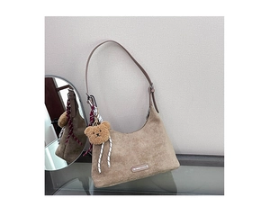 Détail du sac demi-lune en daim fauve avec logo métal, breloque ours et foulard
