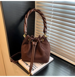 Détail du sac seau en daim marron avec poignée tressée épaisse et accents dorés