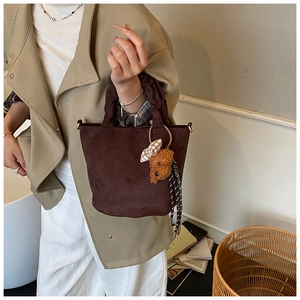 Detail of dark brown suede bucket bag with decorative teddy bear charm and pleated handle