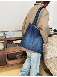 Detailed embroidery of palm trees on a dark blue denim tote bag with frayed edges