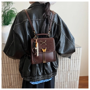 Detail of vintage brown leather backpack with golden butterfly charm and bead tassel charm