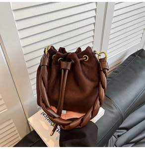 Détail du sac seau en daim marron foncé avec poignée tressée et anneaux en métal doré