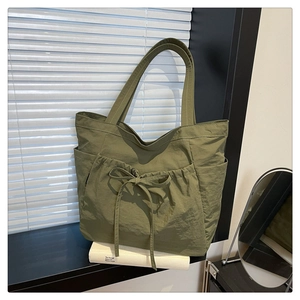 Detailed view of the olive green nylon tote with decorative drawstring bows and side pockets