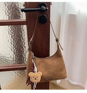 Détail du sac hobo marron avec bandoulière réglable, logo en métal et breloque ours