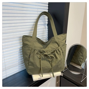 Detail of army green nylon tote bag featuring bow drawstring pocket and side compartments