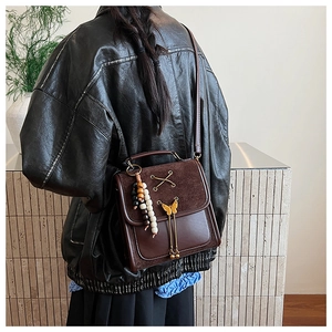 Detailed side view of brown leather crossbody bag with bow hardware and bead tassel