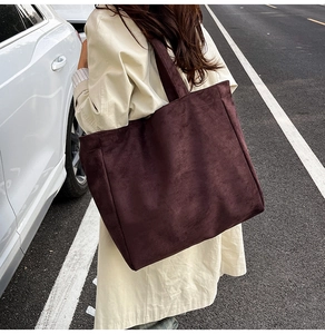 Detail of a large burgundy suede tote bag showing texture and wide shoulder strap