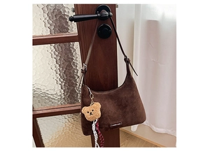 Détail d'un sac Hobo en daim marron foncé avec plaque en métal et breloque ours