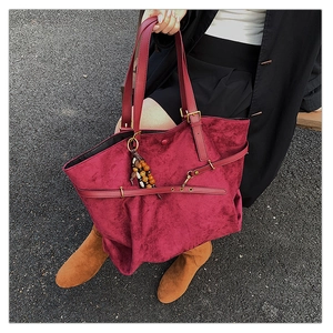Detail of burgundy suede tote bag featuring a leather strap and ethnic bead charm