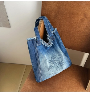 Close-up of denim tote bag showing beach palm tree prints and raw frayed edge details
