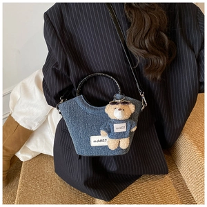 Dettaglio borsa a secchiello in denim con manico tondo nero e ciondolo a forma di orsetto