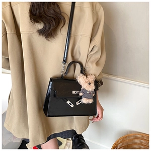 Detail of black leather satchel with silver lock and a cute plush bear charm