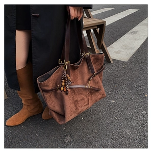 Detail of dark brown suede tote bag featuring adjustable leather straps and wood bead tassel