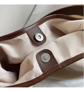 Close-up of premium metal magnetic clasp and leather trim on embroidered canvas tote bag